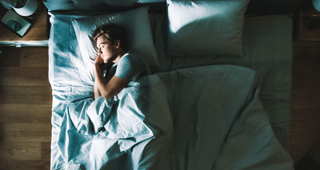 Pessoa dormindo profundamente em ambiente escuro, destacando o sono como fator essencial para acelerar a recuperação muscular após treinos intensos.