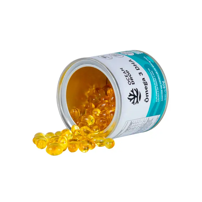 Pote de Ômega-3 da Ocean Drop aberto com cápsulas douradas espalhadas, suplemento usado para foco e equilíbrio inflamatório.