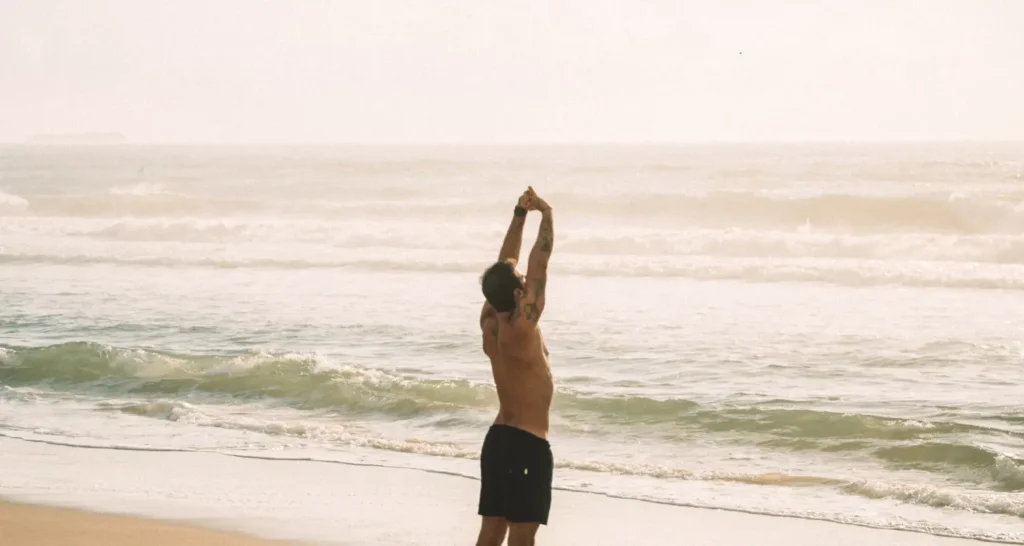 Pessoa realizando alongamento leve na praia como parte de uma rotina para distribuir intensidade e reduzir fadiga acumulada entre treinos.