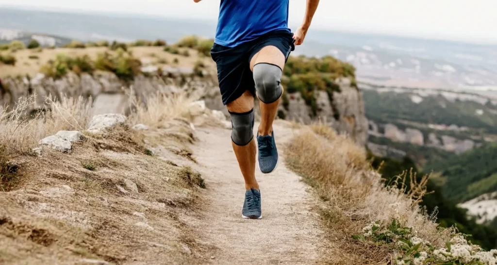 Pessoa correndo em trilha usando joelheira, ilustrando diferentes tipos de suporte para treino e corrida.
