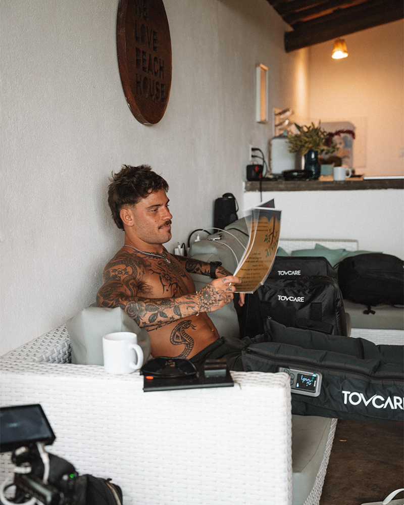 Pessoa usando botas pneumáticas de compressão da Tovcare enquanto relaxa em um ambiente interno e lê uma revista.